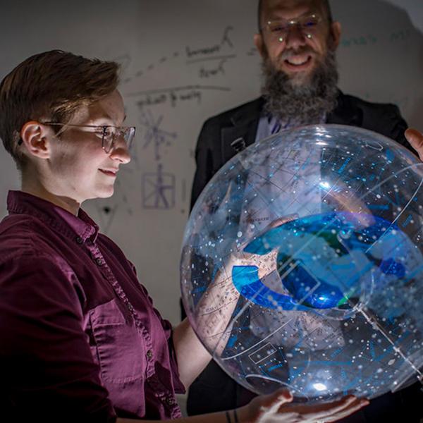 一个学生拿着一个显示星座的地球仪，而一位教授在旁边看着