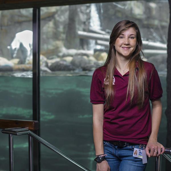 一位年轻女子和一只北极熊站在动物园的展览品前