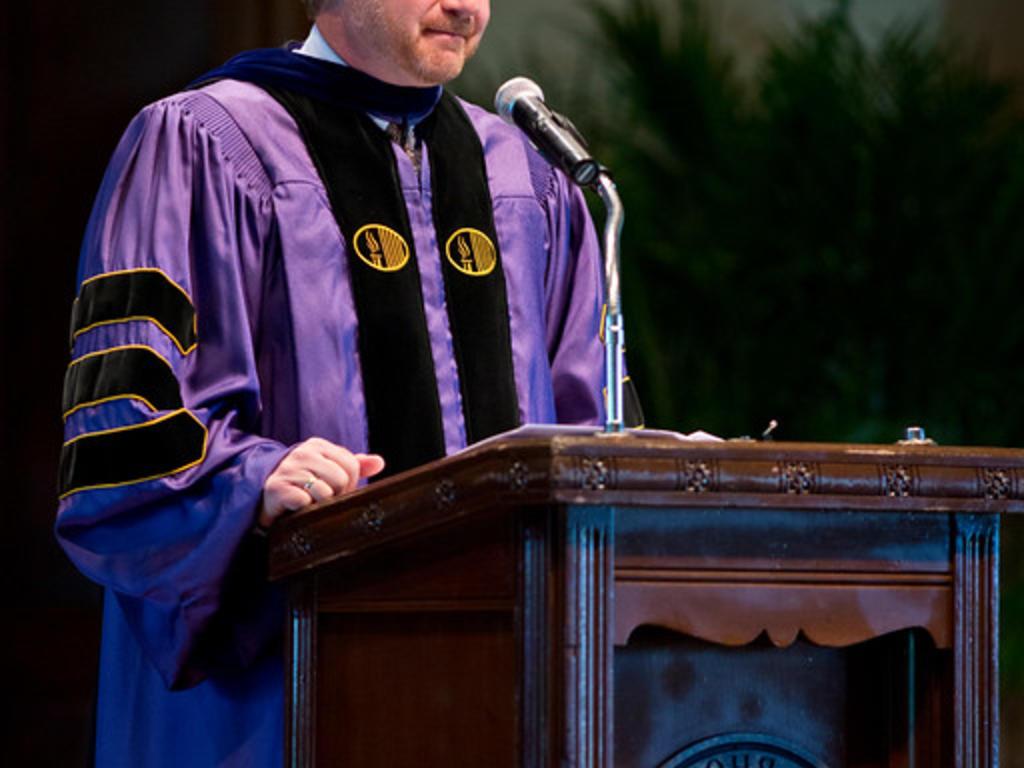 a man in academic robes stands at a lectern